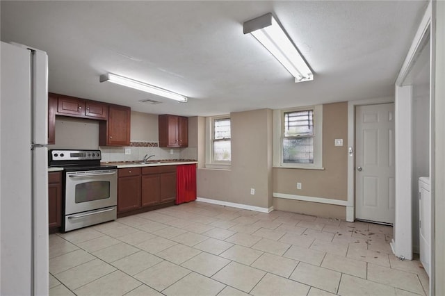 kitchen featuring baseboards, stainless steel electric range, freestanding refrigerator, a sink, and light countertops