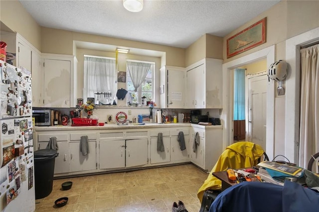 kitchen featuring stainless steel microwave, white cabinets, light countertops, and freestanding refrigerator