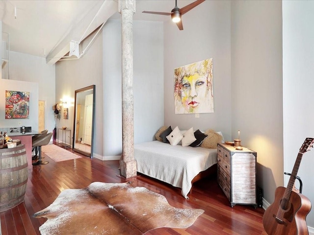 bedroom featuring decorative columns, ceiling fan, a towering ceiling, and dark wood-type flooring