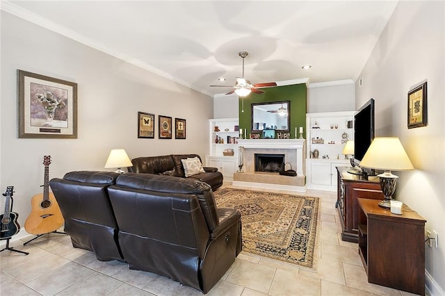 living room featuring crown molding, ceiling fan, a tiled fireplace, built in features, and light tile patterned flooring