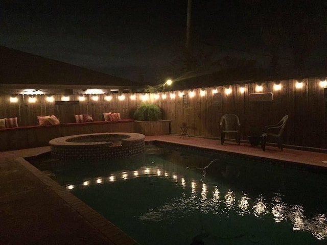 pool at night featuring an in ground hot tub and a patio