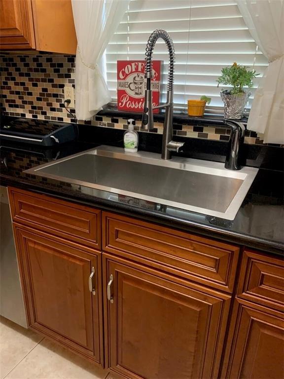 kitchen featuring sink, tasteful backsplash, light tile patterned floors, and dark stone countertops