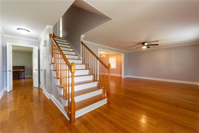 staircase with ceiling fan with notable chandelier, hardwood / wood-style flooring, and crown molding