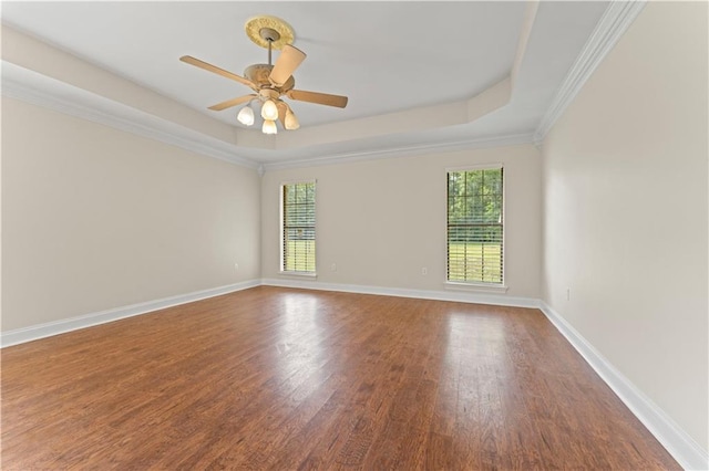 spare room with ornamental molding, wood finished floors, a raised ceiling, and baseboards