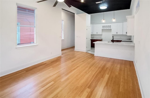 kitchen featuring white cabinetry, sink, ceiling fan, hanging light fixtures, and light wood-type flooring