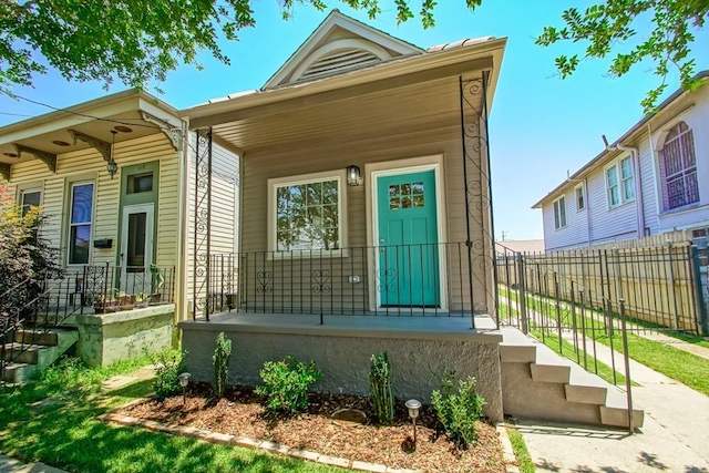 shotgun-style home featuring covered porch and fence