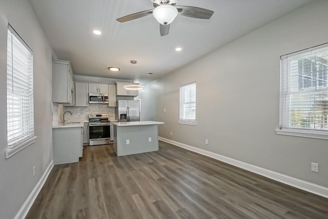 kitchen with light countertops, appliances with stainless steel finishes, hanging light fixtures, backsplash, and a center island