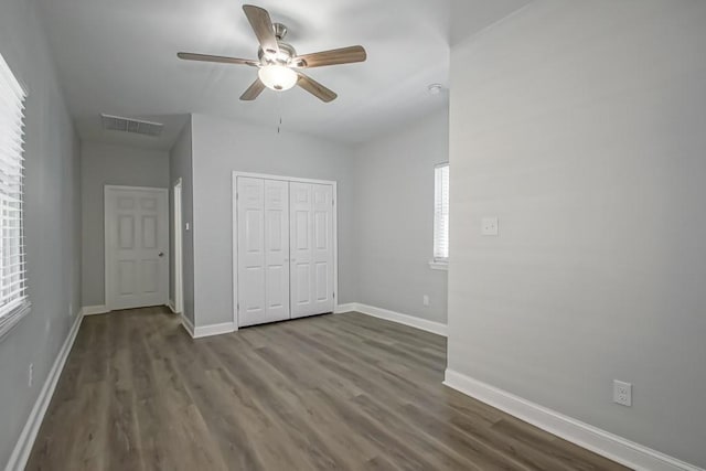 unfurnished bedroom with baseboards, visible vents, dark wood-style floors, ceiling fan, and a closet