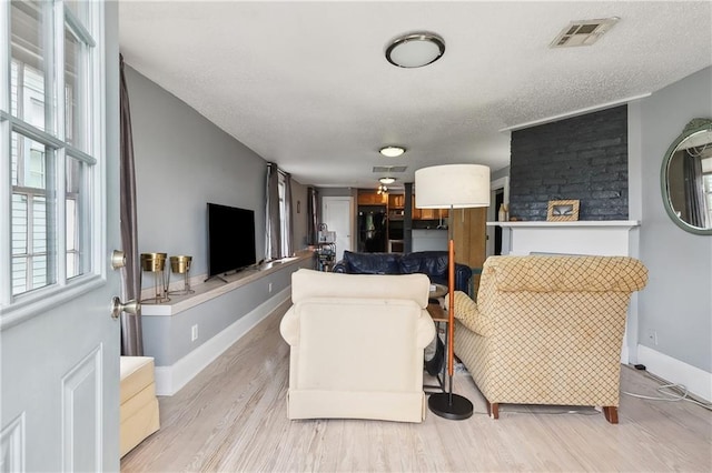 living room featuring a textured ceiling, light wood-type flooring, and brick wall