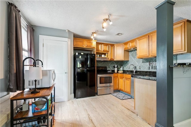 kitchen with dark stone counters, light hardwood / wood-style flooring, stainless steel appliances, a textured ceiling, and backsplash