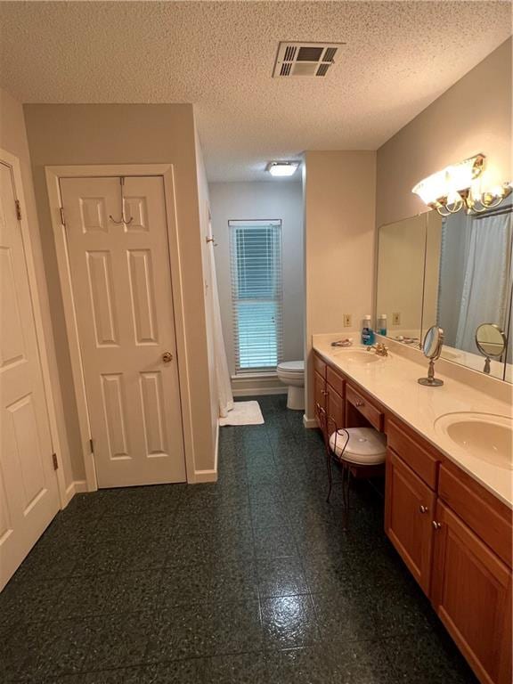 bathroom featuring tile flooring, double sink vanity, toilet, and a textured ceiling