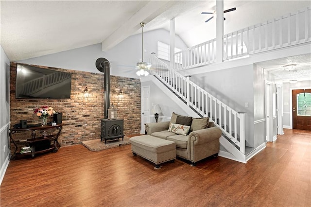 living area featuring beam ceiling, a ceiling fan, wood finished floors, stairs, and a wood stove