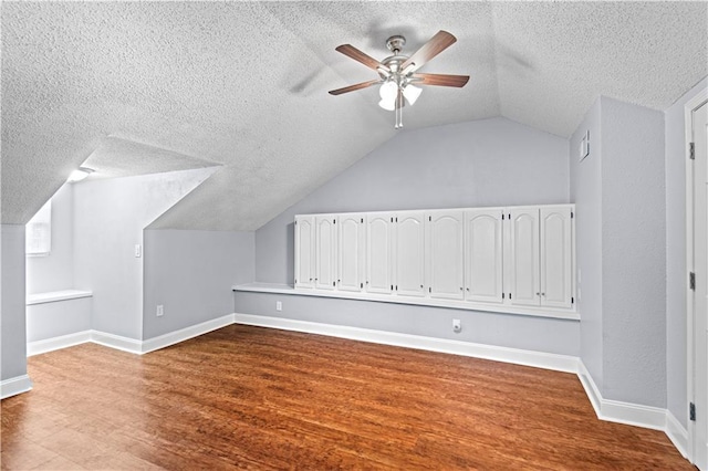 additional living space with vaulted ceiling, a ceiling fan, wood finished floors, a textured ceiling, and baseboards
