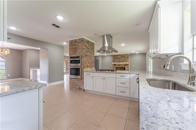 kitchen with a large fireplace, stainless steel appliances, sink, wall chimney range hood, and white cabinets