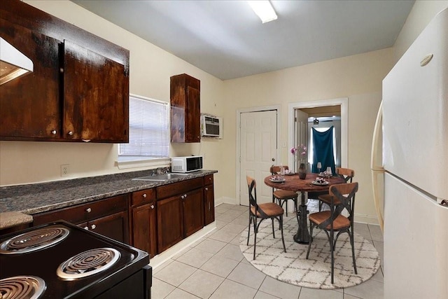 kitchen with light tile patterned floors, white appliances, dark brown cabinetry, and dark stone counters