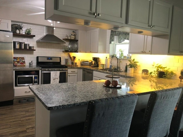 kitchen featuring light stone countertops, appliances with stainless steel finishes, wall chimney range hood, and kitchen peninsula