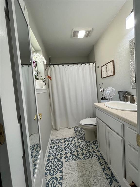 bathroom with vanity, walk in shower, toilet, and tile patterned flooring