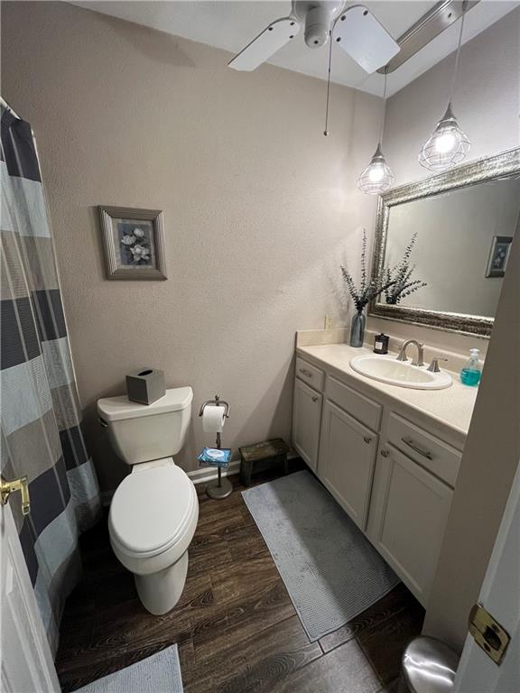 bathroom with toilet, wood-type flooring, a shower with shower curtain, vanity, and ceiling fan