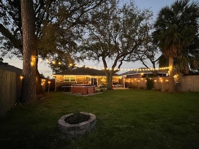 yard at dusk with a hot tub and an outdoor fire pit