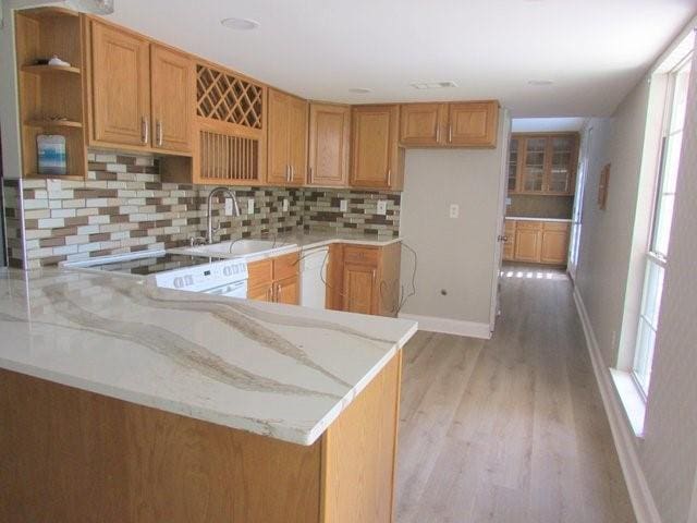 kitchen with kitchen peninsula, light stone countertops, tasteful backsplash, sink, and light hardwood / wood-style floors