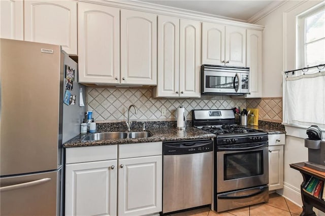 kitchen featuring appliances with stainless steel finishes, ornamental molding, sink, light tile patterned floors, and white cabinetry