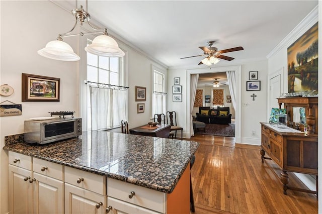 kitchen with dark hardwood / wood-style floors, ornamental molding, hanging light fixtures, and dark stone counters