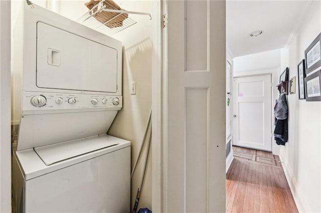 laundry area with light wood-type flooring, stacked washing maching and dryer, and ornamental molding