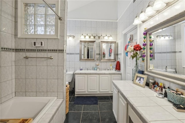 bathroom with a relaxing tiled tub, tile patterned floors, toilet, vanity, and tile walls