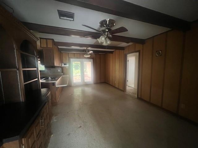 interior space featuring concrete flooring, ceiling fan, wooden walls, beamed ceiling, and french doors