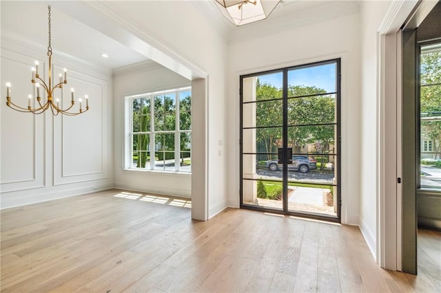 doorway to outside with ornamental molding, light hardwood / wood-style flooring, and an inviting chandelier