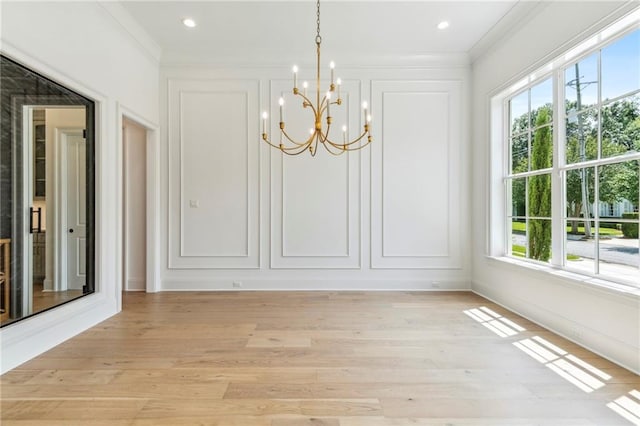 unfurnished dining area featuring light hardwood / wood-style floors, an inviting chandelier, and crown molding