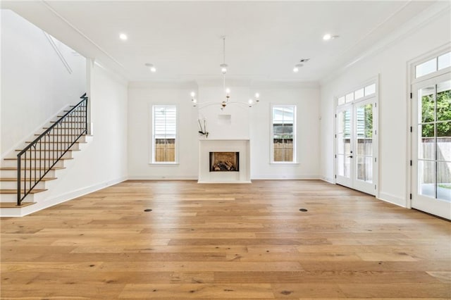 unfurnished living room featuring an inviting chandelier, french doors, light wood-type flooring, and ornamental molding