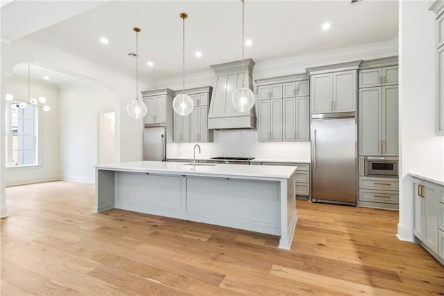 kitchen featuring premium range hood, stainless steel built in refrigerator, hanging light fixtures, and light wood-type flooring