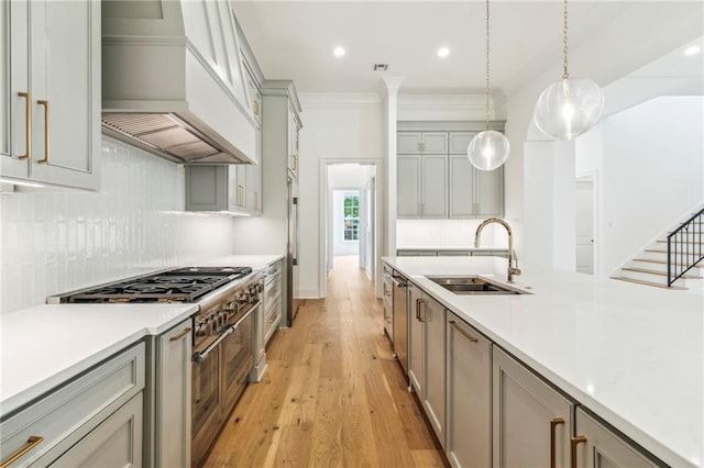 kitchen with tasteful backsplash, light wood-type flooring, premium range hood, hanging light fixtures, and sink