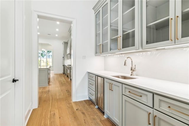 bar featuring gray cabinetry, sink, decorative backsplash, light wood-type flooring, and dishwasher