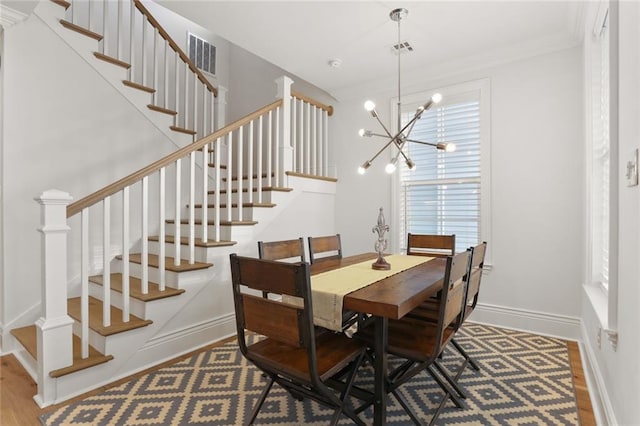 dining space featuring wood-type flooring, a notable chandelier, and crown molding