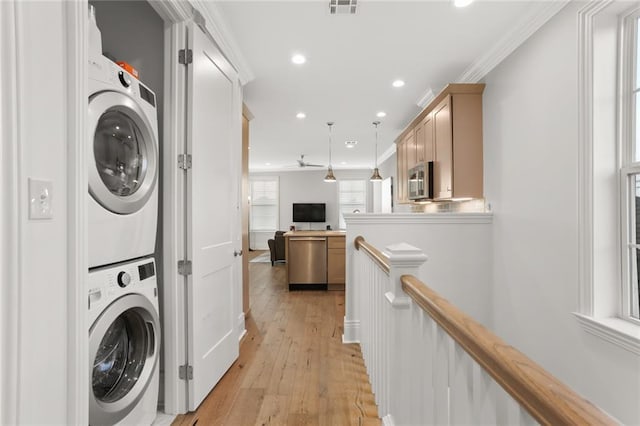 clothes washing area featuring crown molding, light hardwood / wood-style flooring, and stacked washing maching and dryer