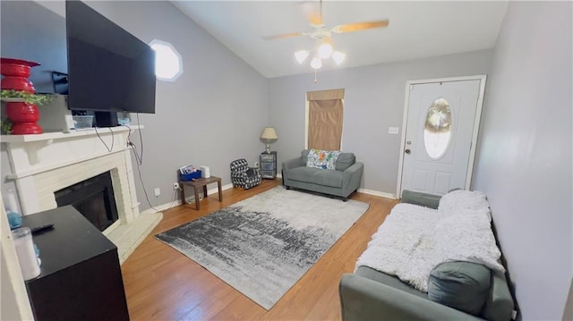 living room featuring a fireplace, light hardwood / wood-style floors, vaulted ceiling, and ceiling fan