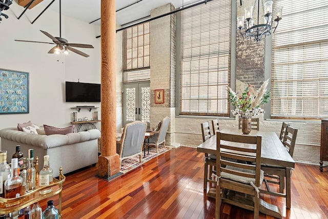 dining room with a high ceiling, hardwood / wood-style flooring, brick wall, and ceiling fan with notable chandelier