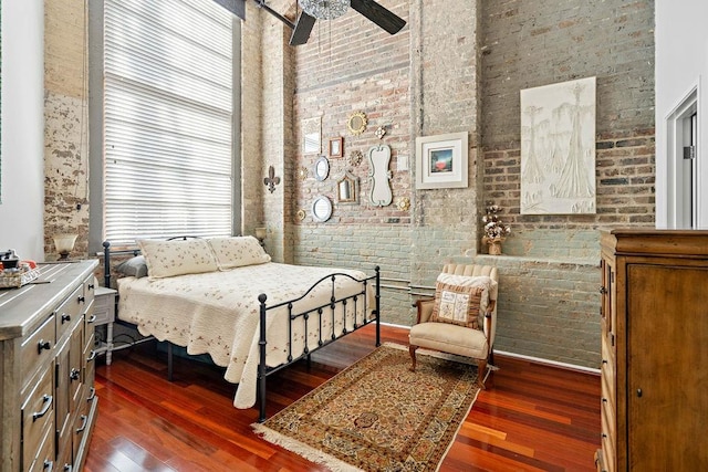 bedroom featuring a towering ceiling, dark wood-type flooring, brick wall, and ceiling fan