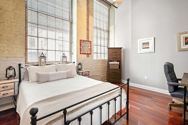 bedroom featuring a towering ceiling, multiple windows, and dark hardwood / wood-style flooring