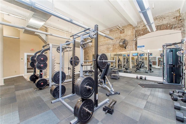 exercise room with a towering ceiling and brick wall