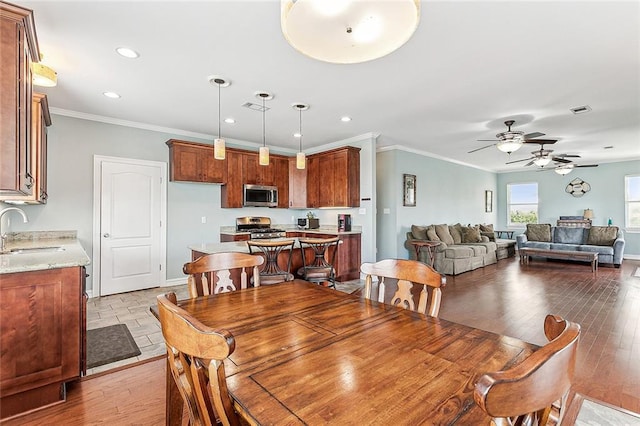 dining space featuring ceiling fan, sink, light wood-type flooring, and crown molding