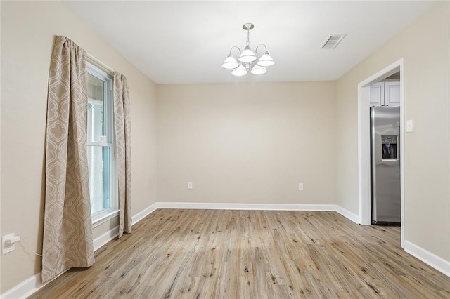 empty room with light hardwood / wood-style floors and an inviting chandelier