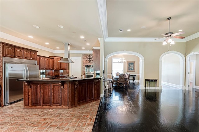 kitchen featuring ceiling fan with notable chandelier, crown molding, an island with sink, island range hood, and stainless steel appliances