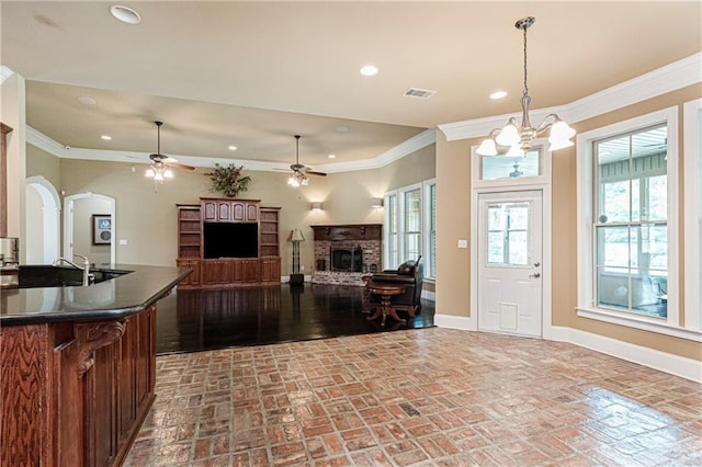 kitchen with a fireplace, hanging light fixtures, ceiling fan with notable chandelier, and ornamental molding