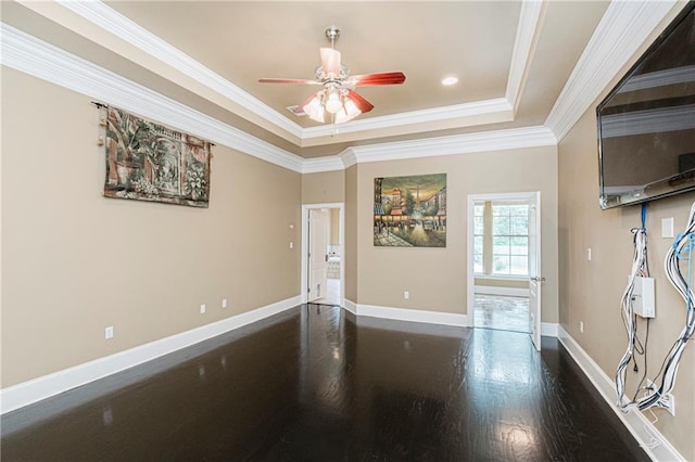 empty room with a raised ceiling, ceiling fan, dark hardwood / wood-style floors, and ornamental molding