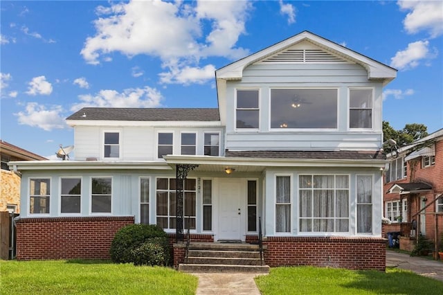 view of front of home featuring a shingled roof, a front yard, and brick siding