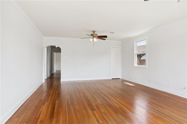 empty room with arched walkways, ceiling fan, dark wood-type flooring, baseboards, and ornamental molding