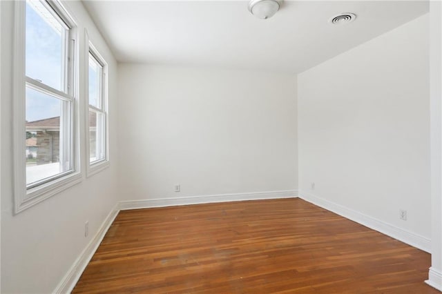 unfurnished room featuring dark wood-type flooring, visible vents, and baseboards